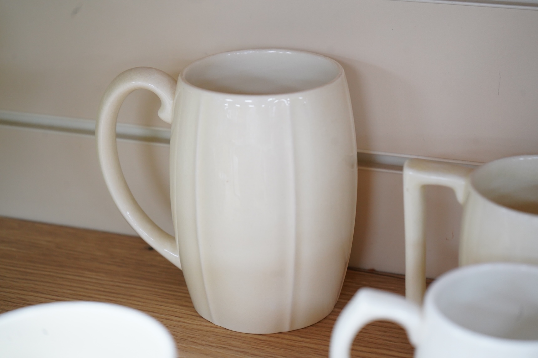 Keith Murray for Wedgwood, a cream lemonade jug, five small mugs, two large three faceted, largest 21cm high (12)